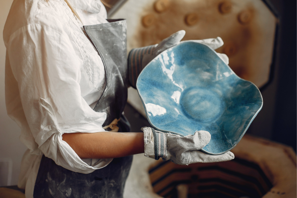Ceramista segurando tigela artesanal de cerâmica azul com formato orgânico irregular, recém-retirada do forno, em ateliê de olaria
