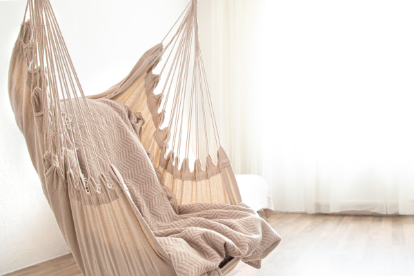 Rede cadeira suspensa de algodão natural em tons bege, com franjas e textura trançada artesanal, em interior minimalista com luz natural difusa
