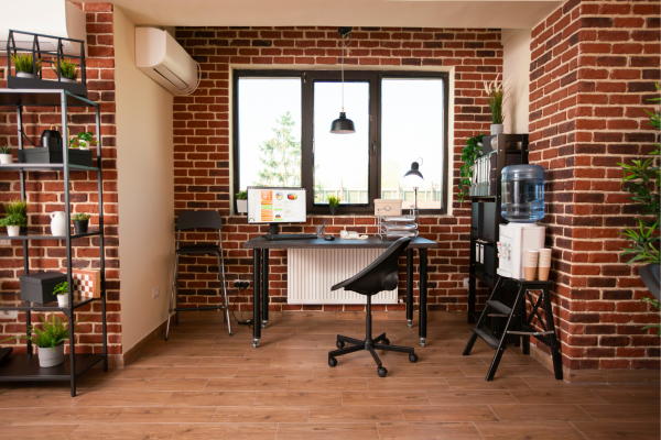 Home office em loft urbano com parede de tijolo aparente vermelho, mobiliário metálico preto, luminária pendente industrial e estantes com plantas, combinando estética pós-industrial e funcionalidade